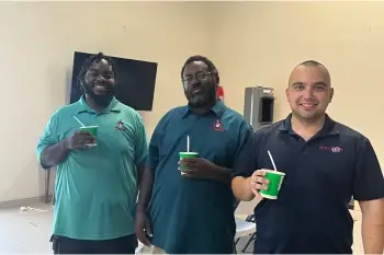 Three smiling men in Willard shirts hold green drinks.