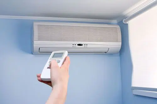 Homeowner adjusting temperature setting of ductless mini-split on a light blue wall. 