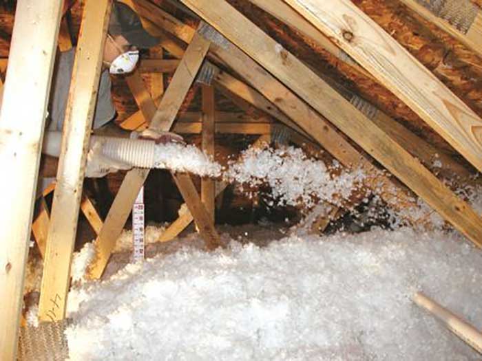 Technician installing blown-in loose-fill insulation in an unfinished attic.