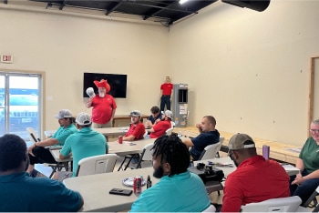A Willard employee in a red gnome hat speaks to the team.