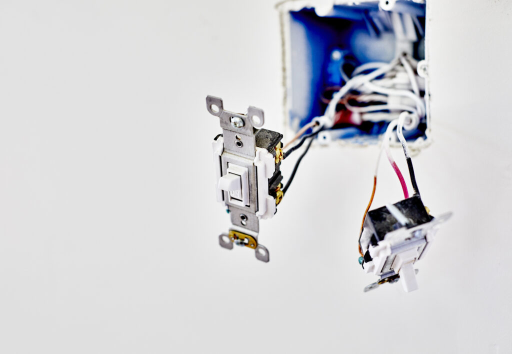 Two light switches hanging from their wires in an open hole in a white wall