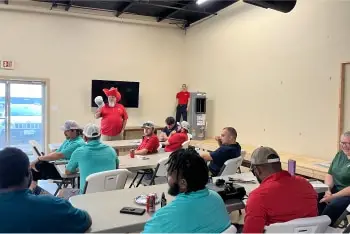 A Willard employee in a red gnome hat speaks to the team.