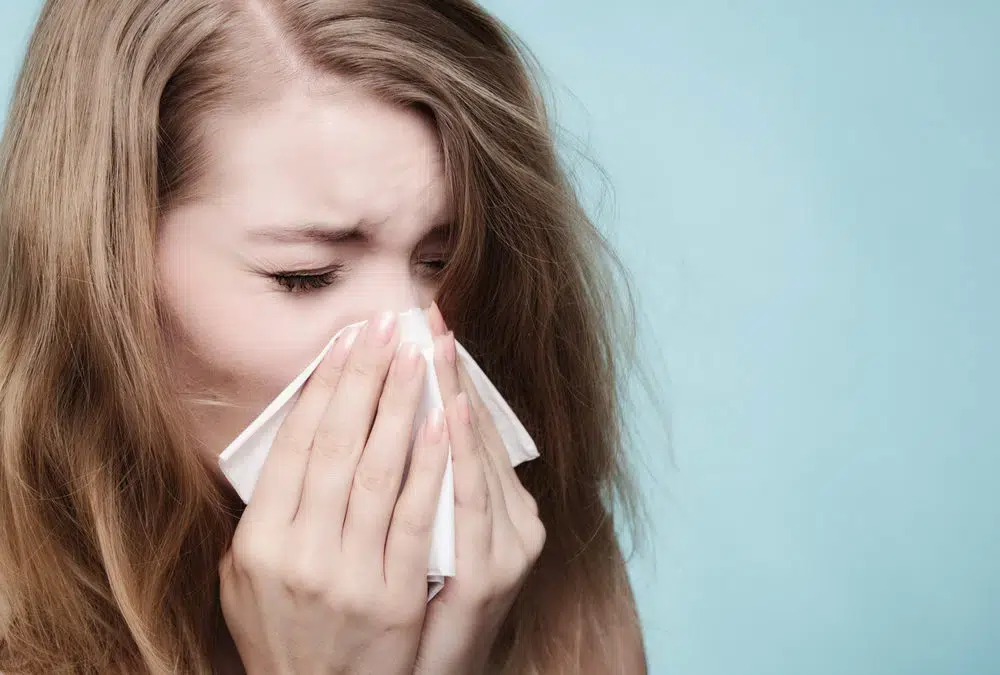  Woman sneezing into tissue as a result of poor attic insulation. Pale blue background. 